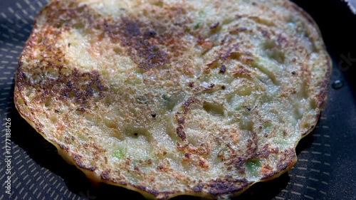 Indian chilla or uttapam prepared on black pan in kitchen with sunlight