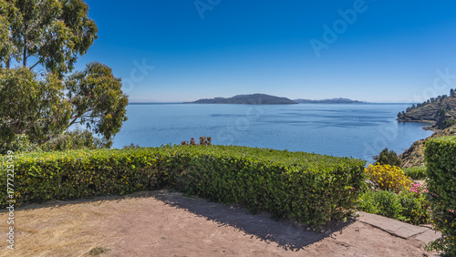 A viewing platform overlooking a beautiful blue lake. A hedge of trimmed bushes, flowers, trees. Mountains on the horizon. Clear azure sky. Peru. Lake Titicaca. Taquile island 