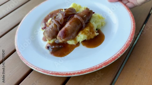 Serving a Plate of Bangers and Mash ( British Sausages and Mashed Potatoes with onion Gravy)