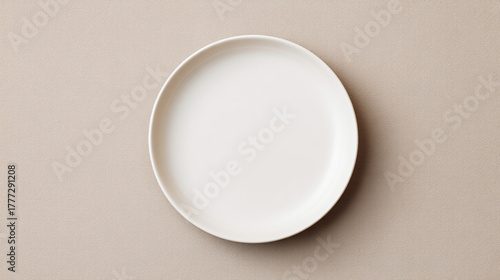 A simple white ceramic plate centered on a light beige background in a studio setting with soft lighting