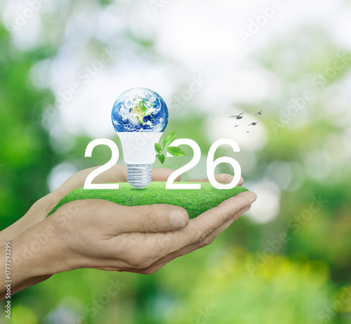 Fototapeta Naklejka Na Ścianę i Meble -  2026 white text and earth globe inside led light bulb with leaves on grass in hands over blur forest, Happy new year 2026 green ecology and saving energy, Elements of this image furnished by NASA