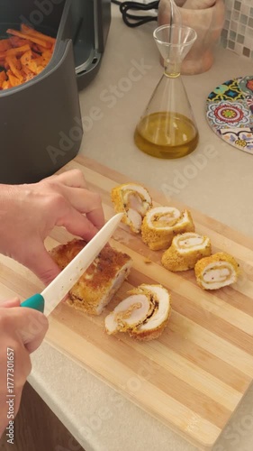 Anonymous person slices baked chicken breast cooked in air fryer into pieces on kitchen counter. Farm produce, food, recipes. Modern technology, innovative appliances. New technologies.