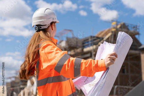 Builder woman working on construction site and using drawings to check works progress