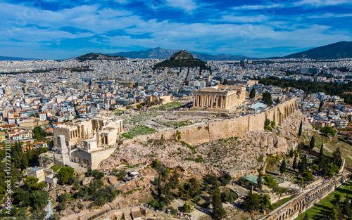 Wide aerial view of the Acropolis, Parthenon, and the ancient Odeon rising above the sprawling modern Athens cityscape.