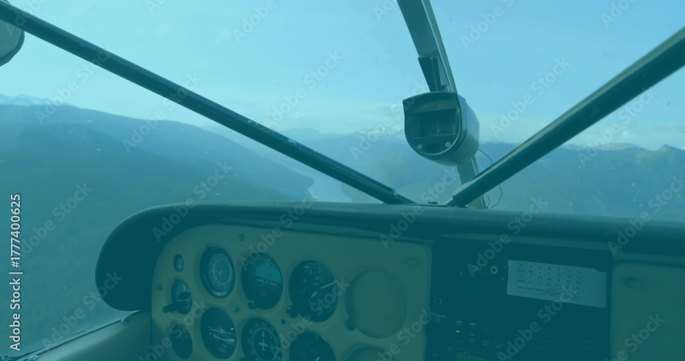 Obraz premium Cockpit panel showing analog gauges in flight framing mountain lake, with radio stack and camera