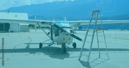 Resting small single-engine propeller aircraft on concrete apron, with aluminum ladder and hangar