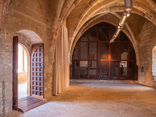 Castell de Bellver, Mallorca, spacious, arched stone hall features a wooden door with intricate lattice work, leading to a large window with similar design elements, Majorca