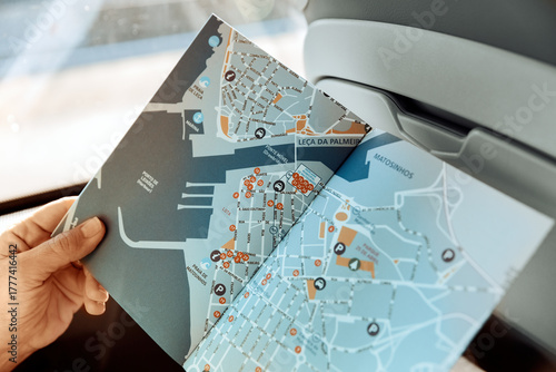 A close-up view inside a coach bus shows a female hand holding a detailed map of Porto's urban and coastal areas, illustrating travel planning on the go. Travel Europe concept.