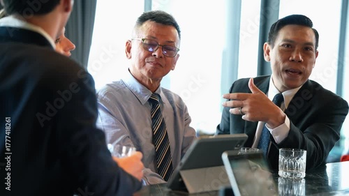Asian businessmen collaborating in an informal corporate meeting, discussing successful business strategy and reviewing financial data on a digital tablet at hotel lounge