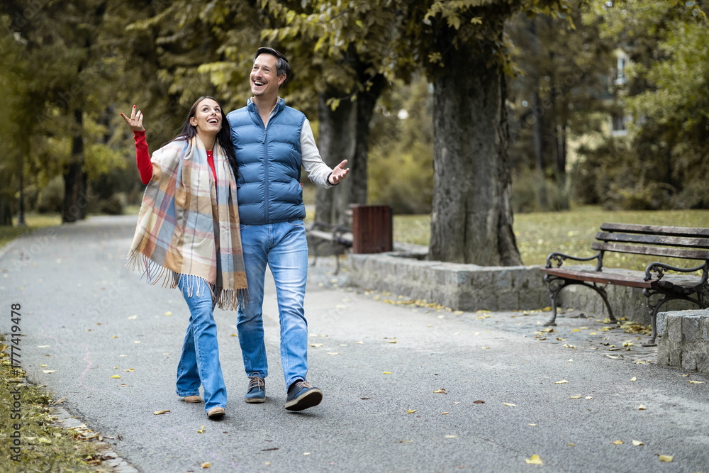Obraz premium The couple is engaged in a lively discussion while walking hand in hand, radiating positivity and joy, surrounded by the vibrant colors of nature in an autumn setting.