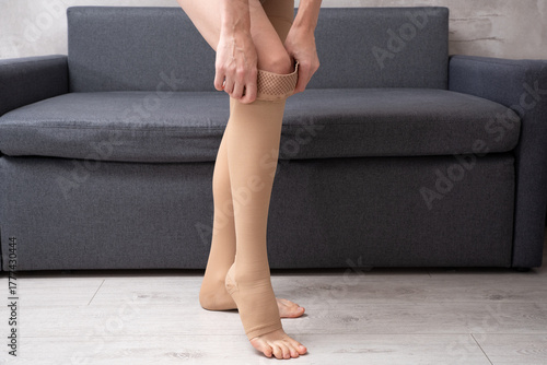 Foto Anonymous woman dressing legs in elastic compression hosiery at home interior pr
