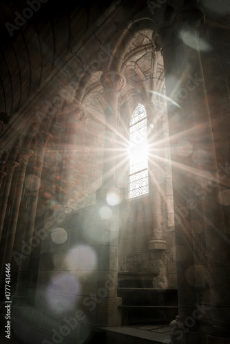 Black and white image of gothic arched stained glass windows inside Mont Saint Michel, with sunlight beaming through the glass and casting rays across the historic stone architecture
