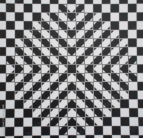 Abstract geometric optical illusion featuring a black and white checkered pattern with layered triangular shapes forming a star-like center. strong visual depth and dynamic symmetry effect.