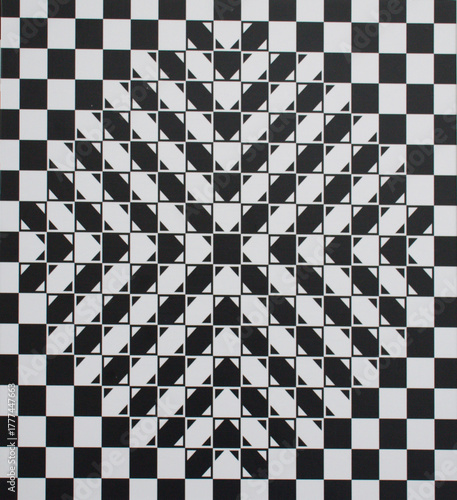 Abstract geometric optical illusion featuring a black and white checkered pattern with layered triangular shapes forming a star-like center. strong visual depth and dynamic symmetry effect.