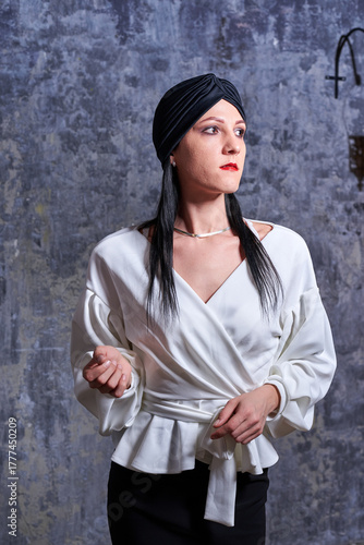 In a dark room stands a beautiful girl with long hair, dressed in a black leather skirt and a white blouse. Her outfit is designed in a business style. This is the image of a business woman.