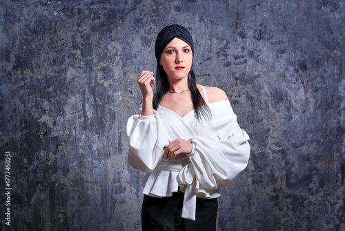 In a dark room stands a beautiful girl with long hair, dressed in a black leather skirt and a white blouse. Her outfit is designed in a business style. This is the image of a business woman.