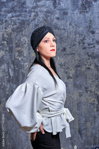 In a dark room stands a beautiful girl with long hair, dressed in a black leather skirt and a white blouse. Her outfit is designed in a business style. This is the image of a business woman.