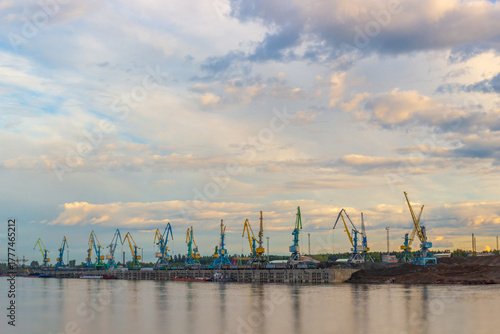 Industrial background with portal gantry cranes at the Lesosibirsk river port on the Yenisei River against cloudy sky background, Russia. Cranes load or unload a freight train