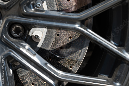 Extreme close-up detail of a perforated carbon-ceramic brake disc, viewed through a black alloy wheel, showing stress cracks from high performance use