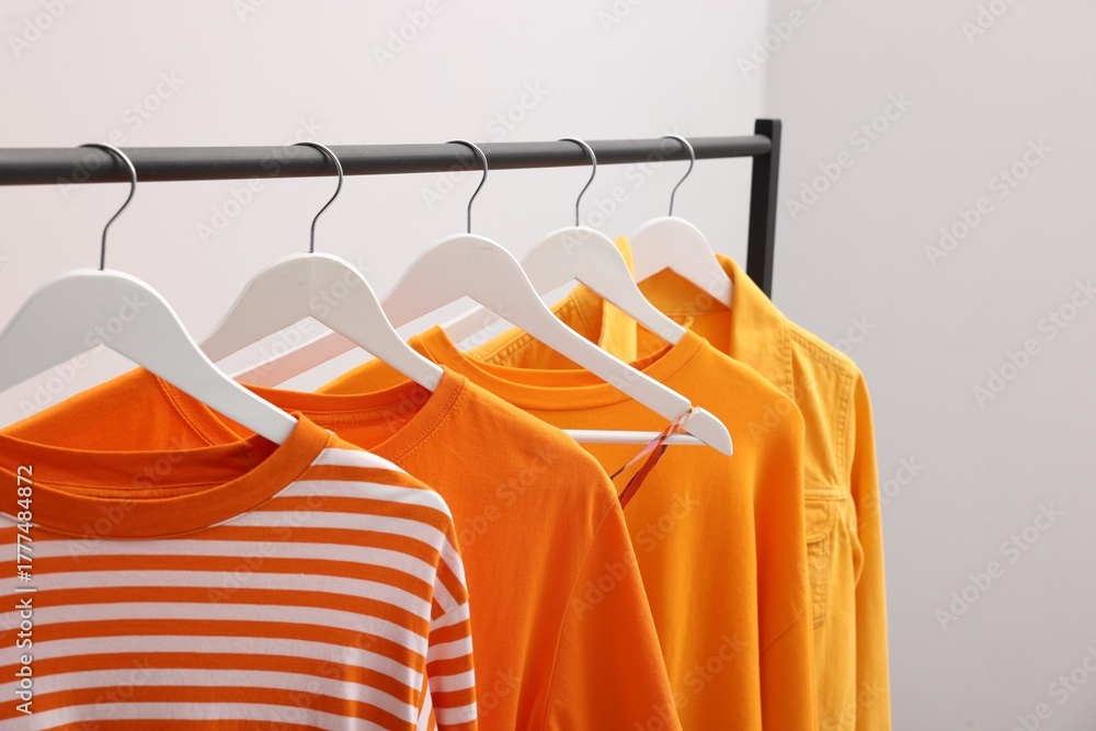 Obraz premium Different stylish clothes hanging on rack near light wall indoors, closeup