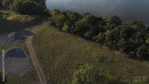 Drone tilts up over dirt path to reveal Neosho River and Lake Hudson near Kerr Dam, Oklahoma