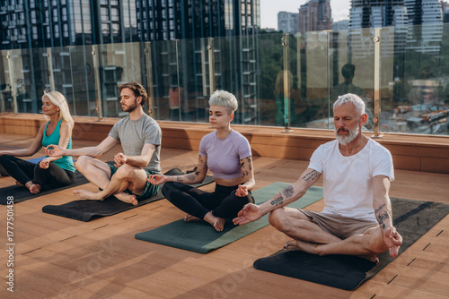 Multiracial people group  meditates together on rooftop against city buildings
