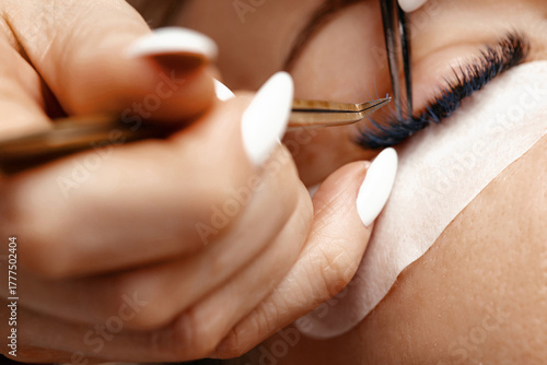 Close-up of a skilled beauty technician applying eyelash extensions with precision tools, showcasing the intricate process of eyelash enhancement and beauty care