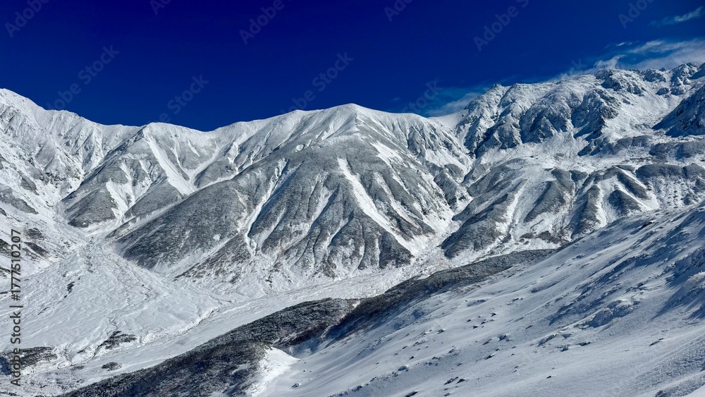 Fototapeta premium Steep Slope and Snowy Mountains under Bright Sky