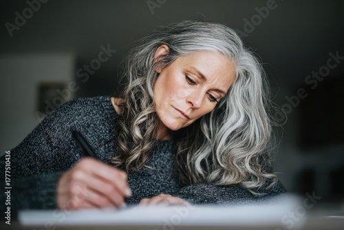 Focused Mature Woman Writing at Desk in Cozy Home Environment.