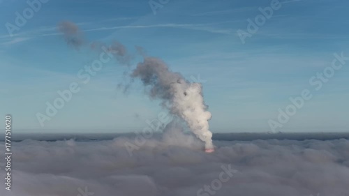 Aerial drone view of industrial chimneys emitting steam above thick fog and clouds on a sunny day, power plant and factory landscape. Panorama above clouds in fog in sunny day. Clouds factory