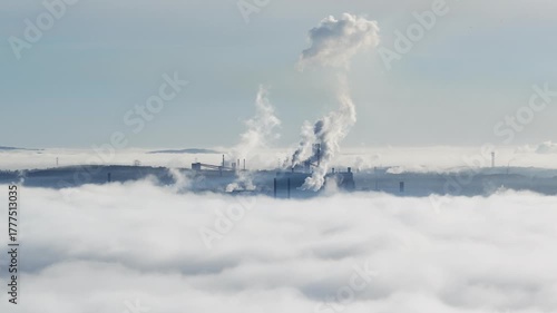 Aerial drone view of industrial chimneys emitting steam above thick fog and clouds on a sunny day, power plant and factory landscape. Panorama above clouds in fog in sunny day. Clouds factory