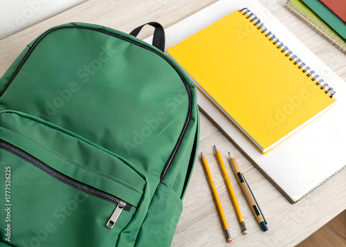 Green backpack with yellow notebook and pencils for school