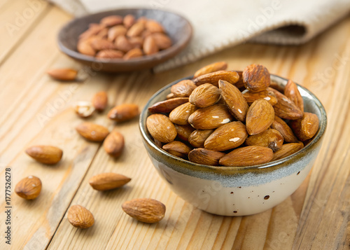 Roasted Almonds in a Bowl with Scattered Nuts on Wooden Table