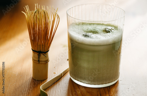 Iced matcha latte with bamboo whisk and spoon on wooden table