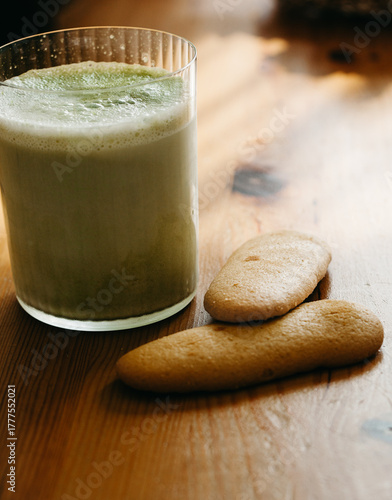 Glass of foamy matcha latte with two sponge biscuits on wooden table