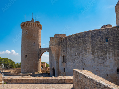 Castell de Bellver, Palma de Mallorca, historic stone castle with a tall cylindrical tower and an arched gateway stands under a clear blue sky, Majorca