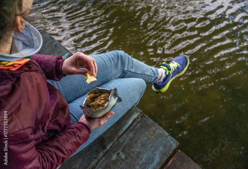 Traveler enjoying outdoor meal near river, camping with healthy dried fruit snack in summer sunlight