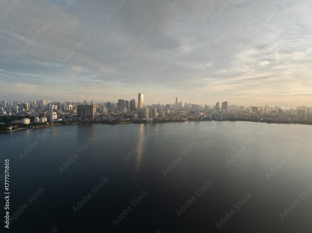 Fototapeta premium Expansive view of West Lake at sunrise with soft light reflecting on calm water and distant city skyline.
