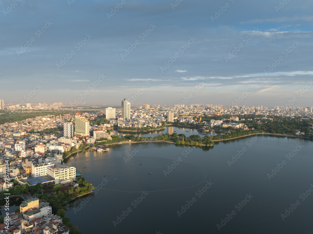 Fototapeta premium Aerial view of West Lake with surrounding urban buildings under clear morning light in Hanoi.