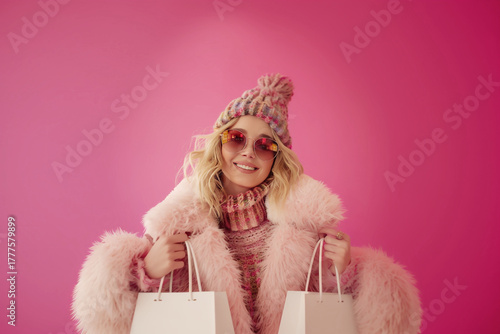 Stylish woman in pink fur coat and hat holding shopping bags against vibrant pink background