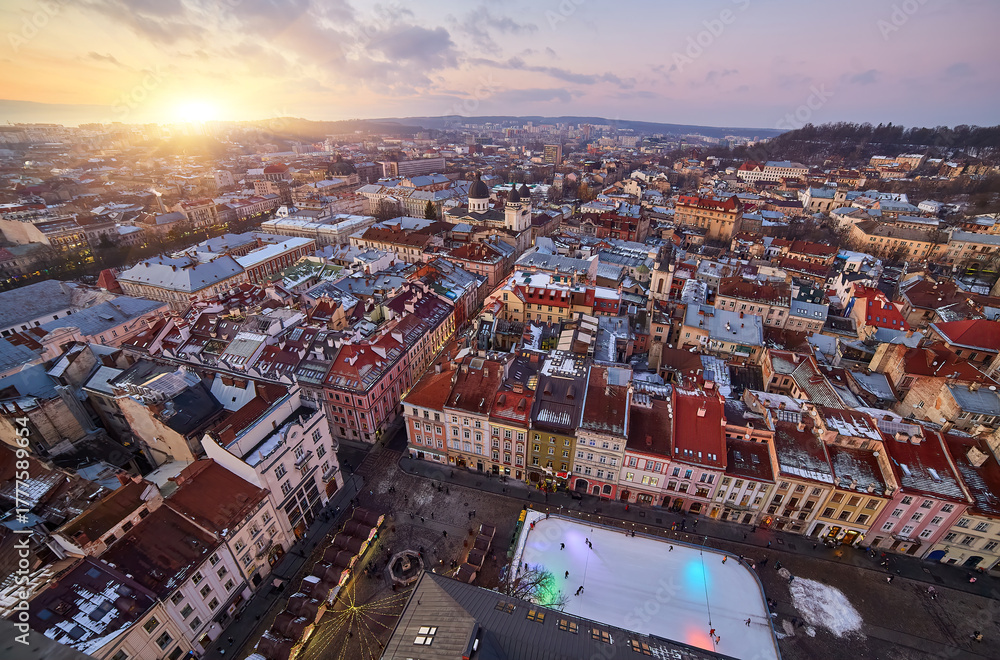 Fototapeta premium Aerial view of a historic European city with snowy rooftops at sunset.