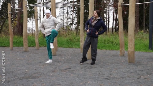 Women practicing sport outdoors on a cool autumn day, performing stretches and warm-up exercises. One is a cancer patient recovering after therapy, symbolizing strength,