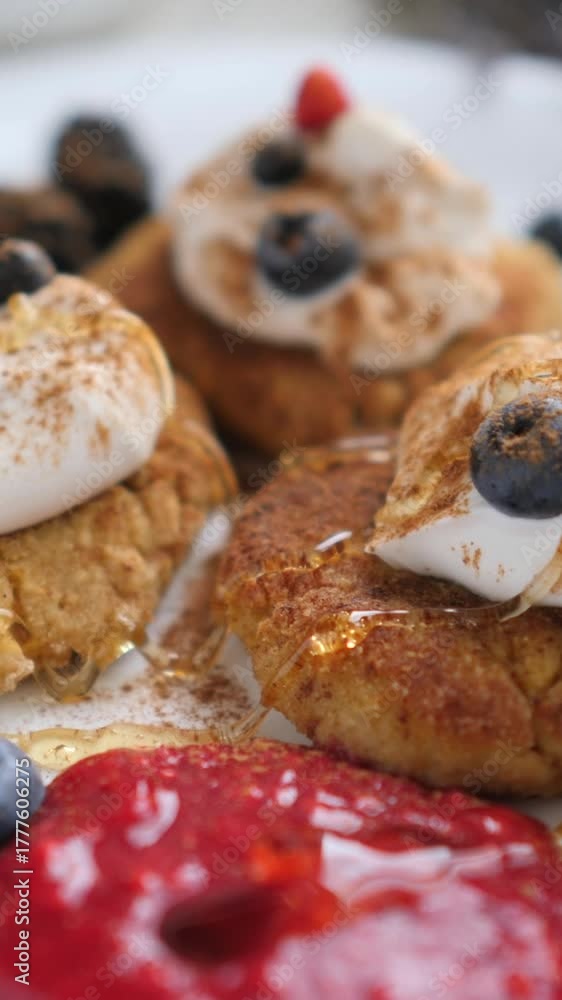 Delicious homemade baked donuts with whipped cream, cinnamon, blueberries, and raspberry jam receiving a drizzle of honey on a white plate in a delectable close up food shot