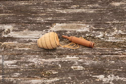 Brazilian wooden spinning top and thrower (batoque), connected by string, displayed on a weathered rustic wooden table. Outdoor setting. Symbolizes traditional Brazilian games, culture, and childhood.