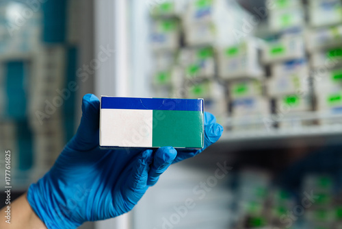 Medical worker holding medicine box with green and blue label. Doctor in gloves displaying medicine package in refrigerator section of pharmacy