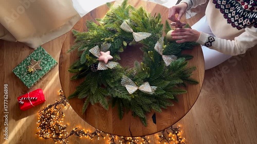 Woman’s hands in a Christmas sweater decorating a festive wreath, top view timelapse, no face visible