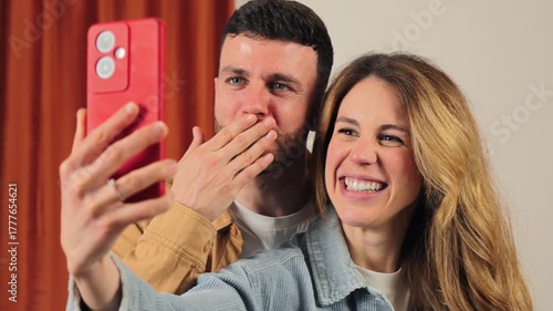 Joyful couple capturing a delightful selfie using their smartphone, sharing smiles and laughter in a moment of happiness and connection, showcasing their affection in a fun way with technology.