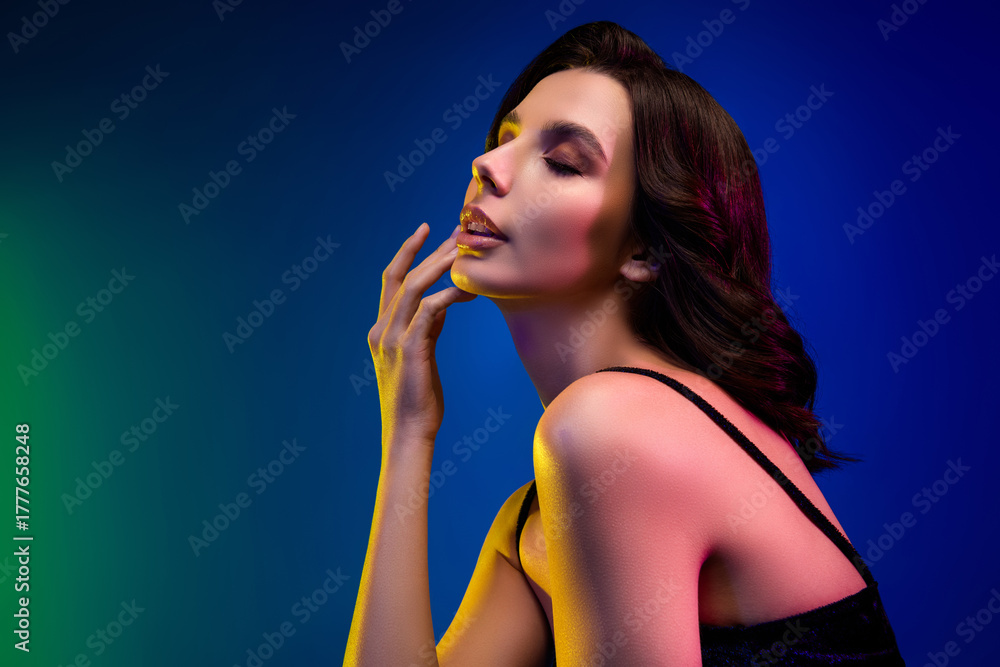 Fototapeta premium Stylish sensual brunette woman posing in neon lighting with vibrant makeup in an elegant dress showcasing beauty