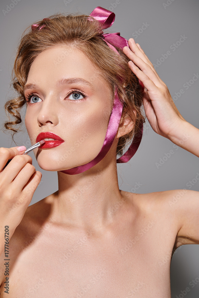Obraz premium Curly-haired woman applies red lipstick, showcasing beauty with pink ribbon charm