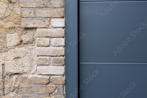 Porte de garage grise anthracite installée par un professionnel, encadrée par un mur en pierre beige et un sol en macadam, entre modernité et authenticité.
